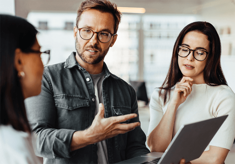 Three office workers looking at a laptop